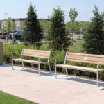 Trois bancs en bois avec une structure métallique, disposés le long d'une allée en béton dans un parc.