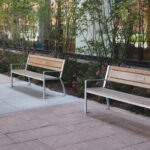 Trois bancs en bois avec une structure métallique, disposés le long d'un trottoir bordé de petits arbustes à fleurs.