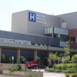 Extérieur du bâtiment de l'hôpital du district de Milton, avec un véhicule d'urgence rouge garé près de l'entrée.