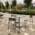 Terrasse de café avec des chaises et des tables en métal, aménagée sur une terrasse pavée de forme hexagonale.