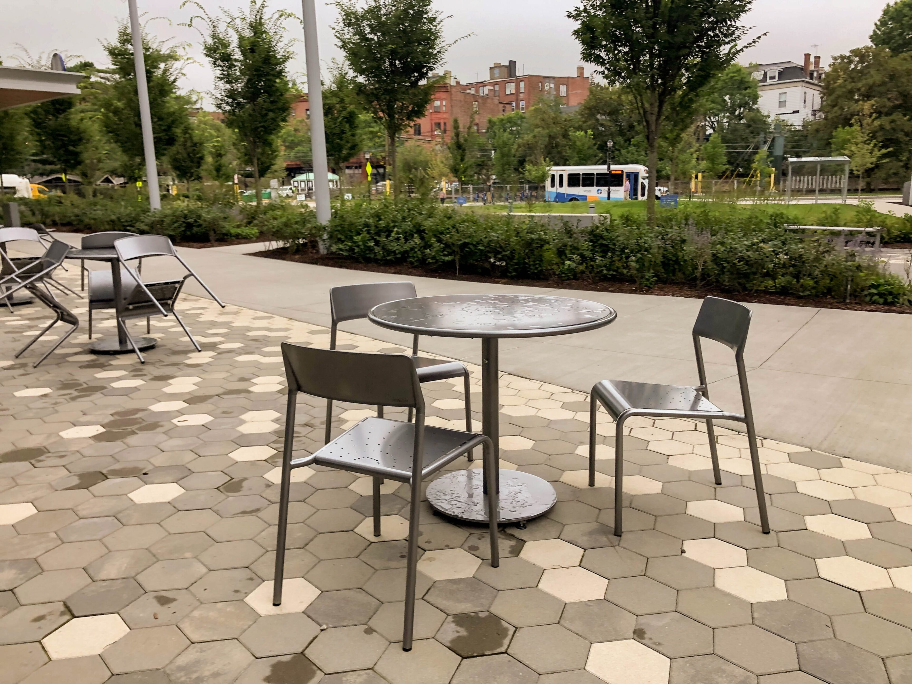 two-brookline-boston-childrens-foro-tables-chairs-2 Terrasse de café avec des chaises et des tables en métal, aménagée sur une terrasse pavée de forme hexagonale.