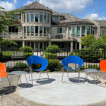 Two blue and two orange modern chairs arranged with small tables on a patio overlooking the VON Sakura House hospice care building.
