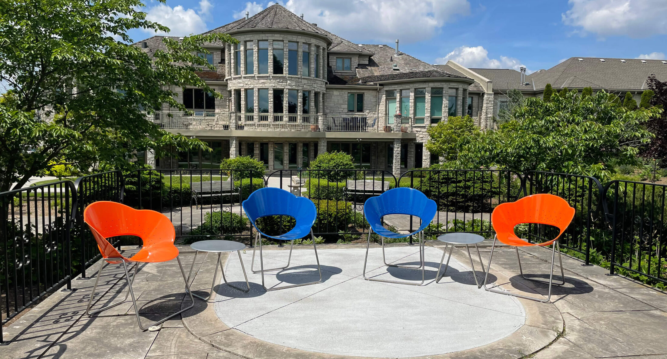 Two blue and two orange modern chairs arranged with small tables on a patio overlooking the VON Sakura House hospice care building.